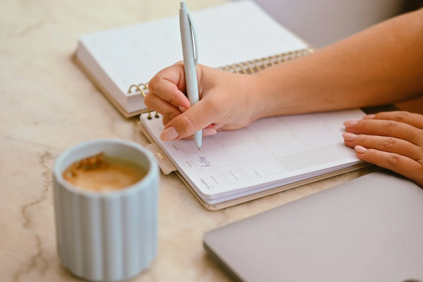 Main qui prend des notes dans un agenda, café sur une table en marbre